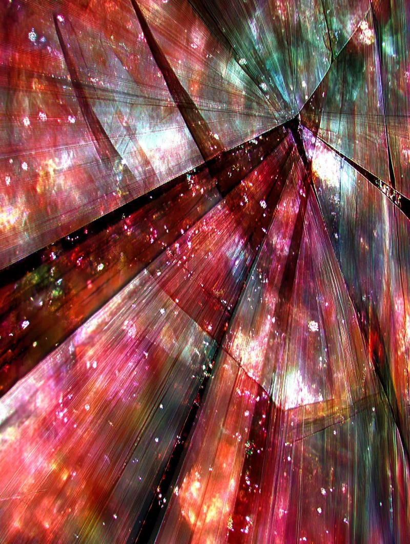 Abstrakcyjna, kolorowa kompozycja przypominająca pęknięte szkło z kosmicznymi światłami i refleksami w odcieniach czerwieni, różu i zieleni.